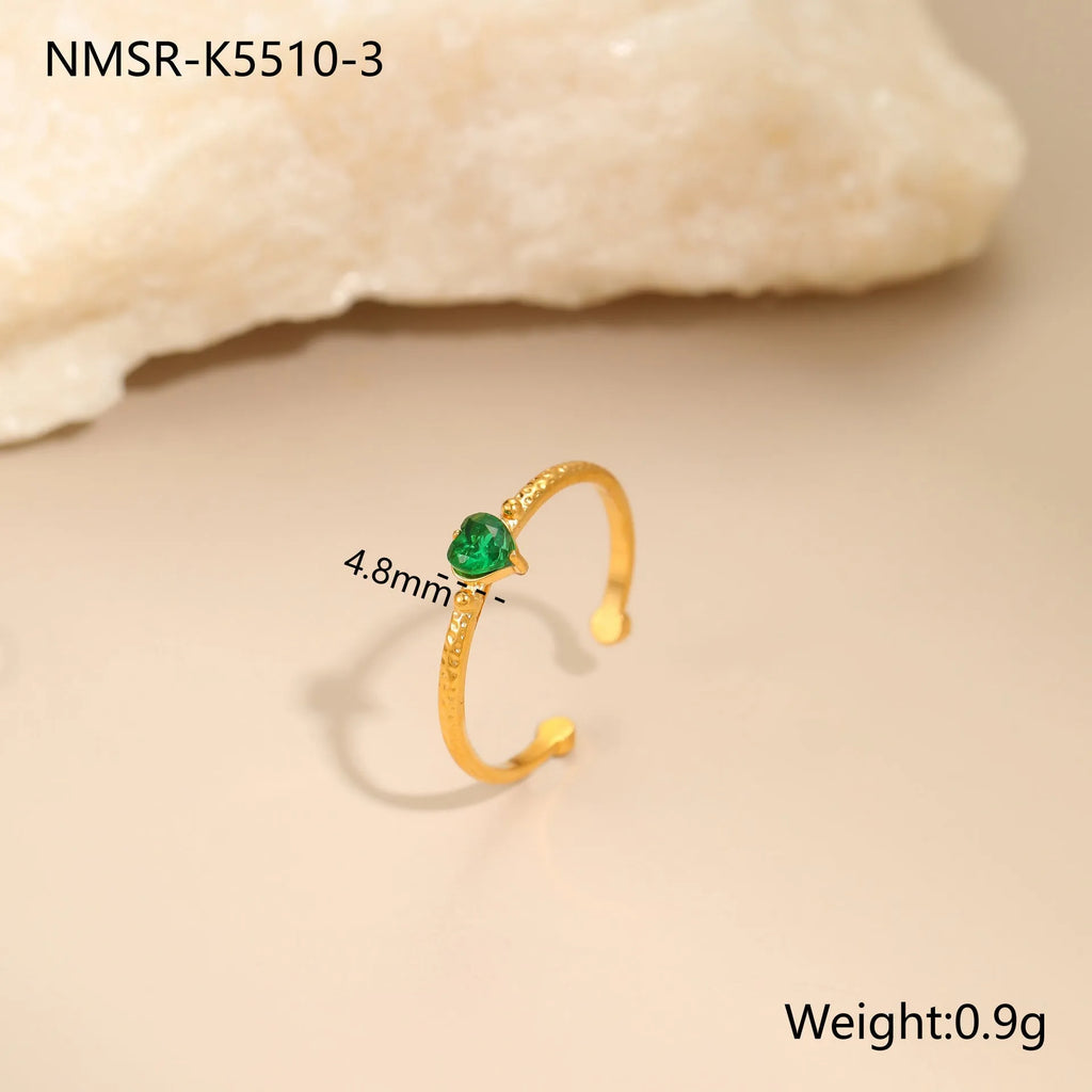 Open-ended stainless steel ring with a geometric heart shape inlaid with green zirconium on a plain background.
