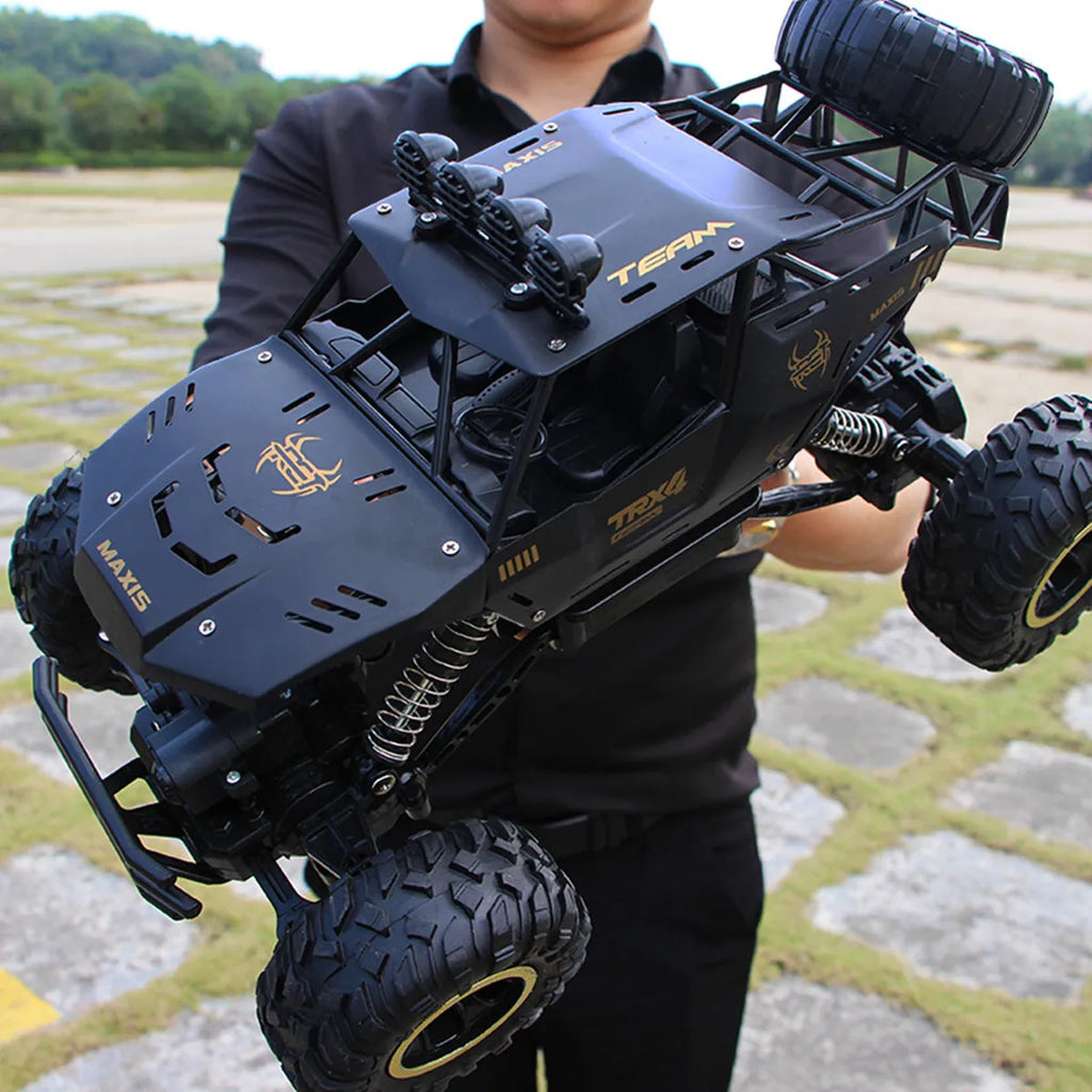 Large black and silver 4WD remote control off-road climbing cars with wireless controller on a rocky surface.