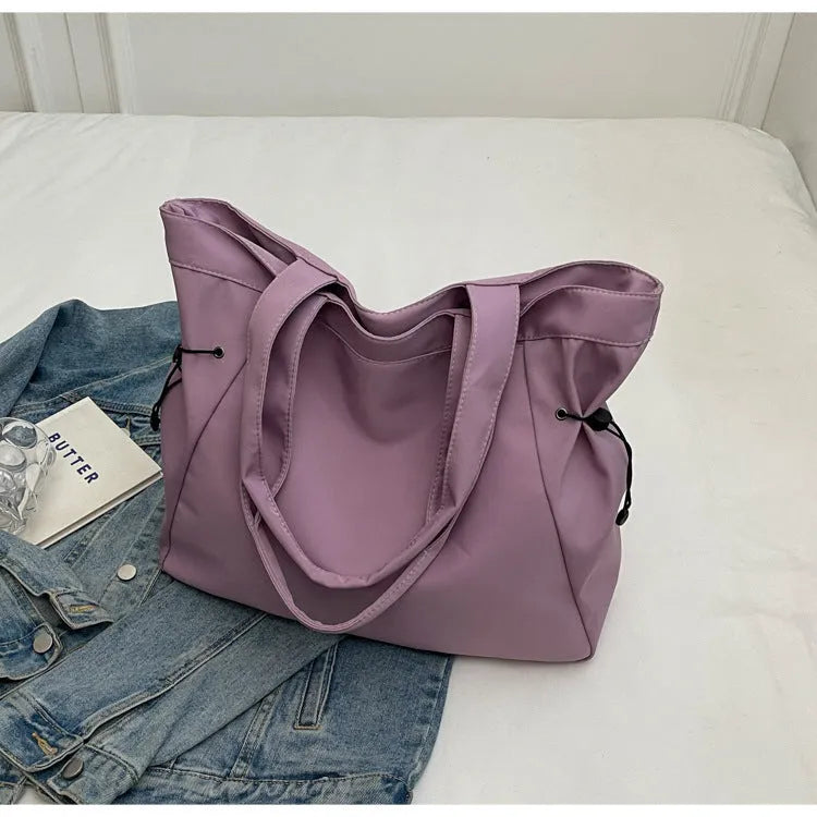 Soft Oxford cloth folding commuter tote bag shown in one of five colours: black, brown, dark grey, light grey or purple.
