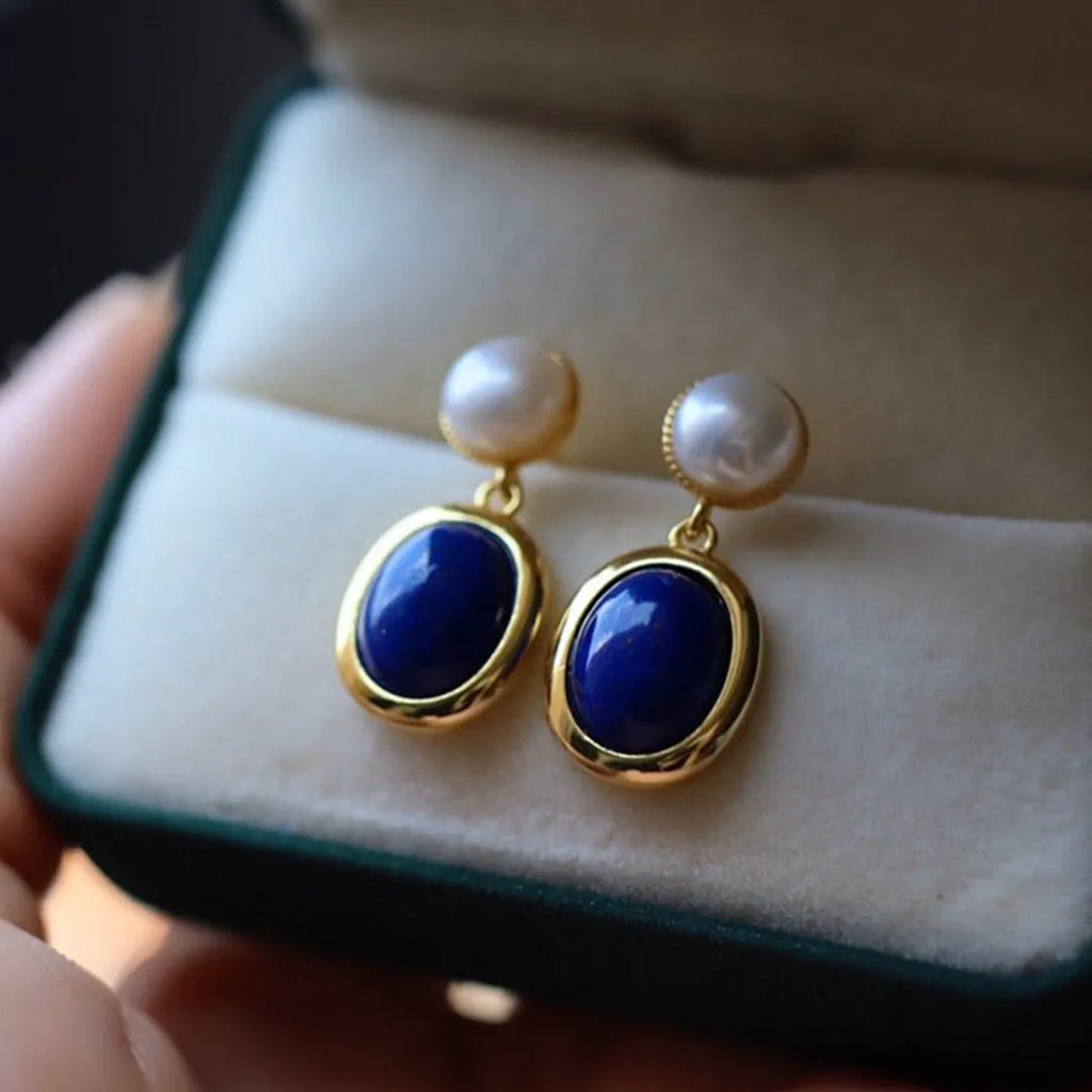 A pair of simple sterling silver stud earrings with blue lapis lazuli pearls and auspicious pattern details.
