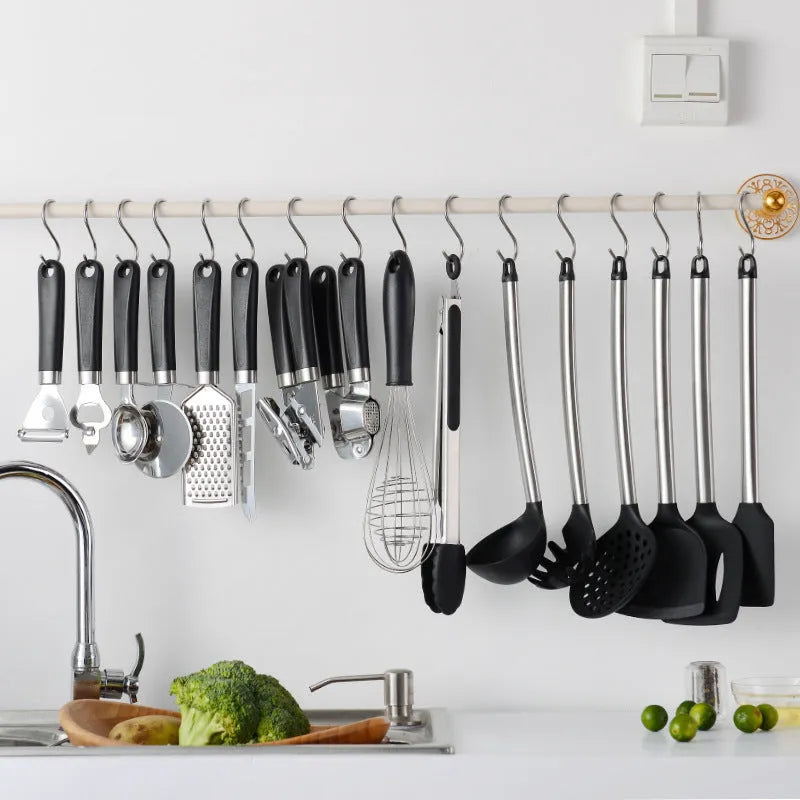 Black silicone and stainless steel kitchen spatula and spoon set, 16 pieces laid out.