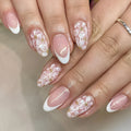Short almond-shaped false nails with French style tips and glittering pink powder flowers on a white background.