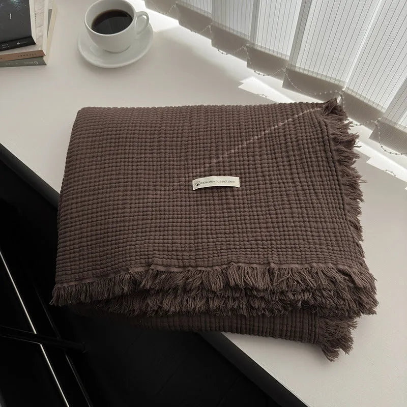Four-layer cotton gauze blanket with tassel trim in avocado green colour laid flat.