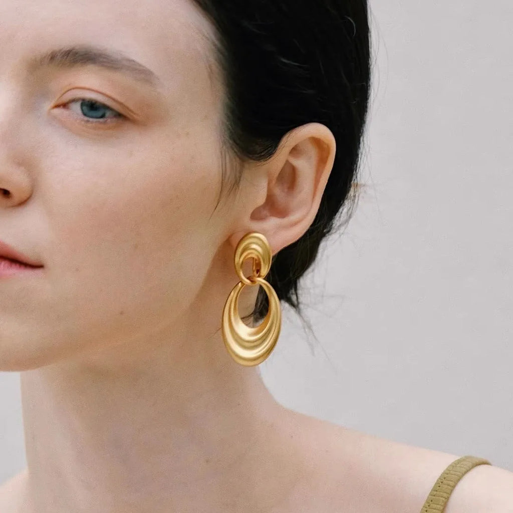 Plain gold coloured U-shaped double circle earrings with a French retro style on a copper background.