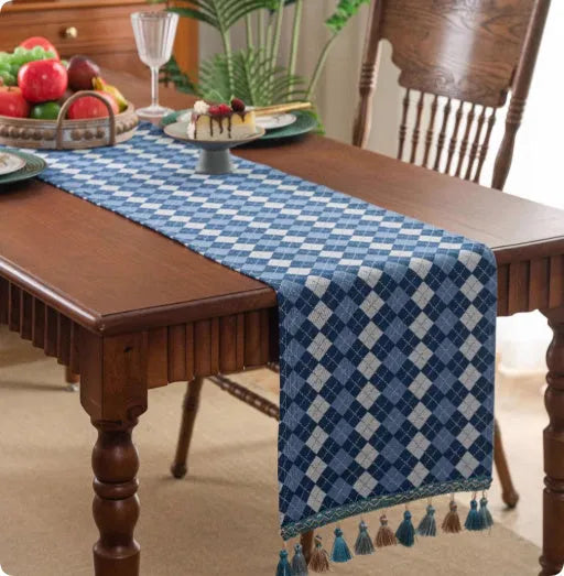 Long decorative table runner with handwoven tassels in a blue ginkgo leaf pattern on a wooden table.