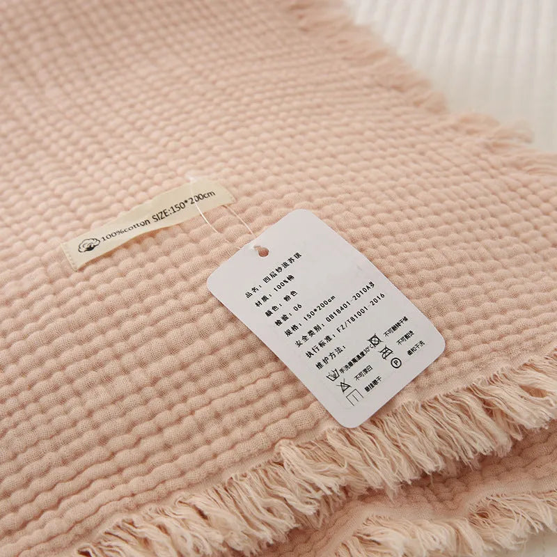 Four-layer cotton gauze blanket with tassel trim in avocado green colour laid flat.