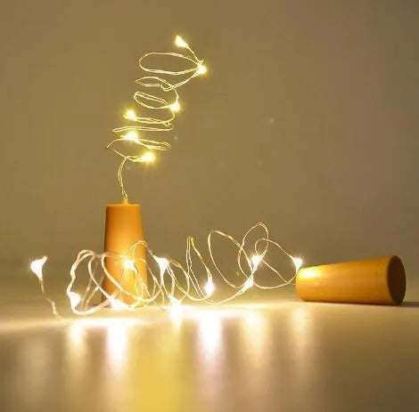 Copper wire LED string light with bottle stopper illuminated in a glass wine bottle.