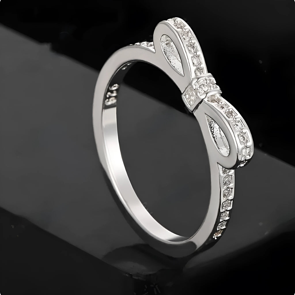 Silver bow-shaped ring with zircon crystals on a finger, showing detailed bow motif design