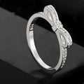 Silver bow-shaped ring with zircon crystals on a finger, showing detailed bow motif design