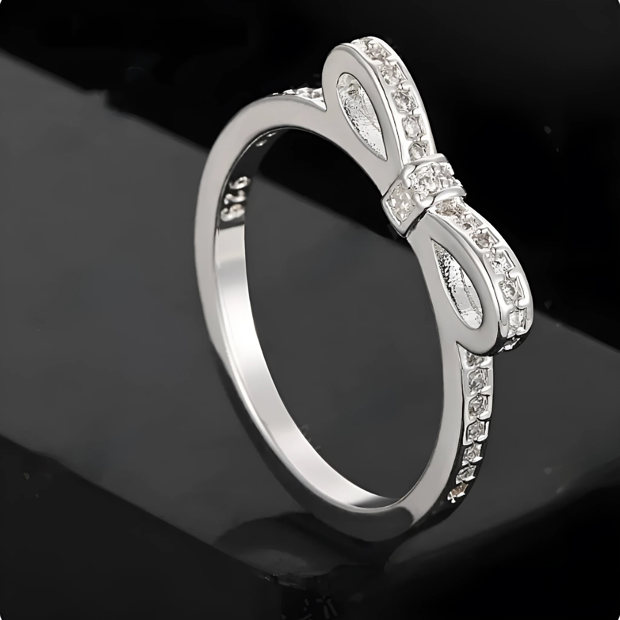 Silver bow-shaped ring with zircon crystals on a finger, showing detailed bow motif design