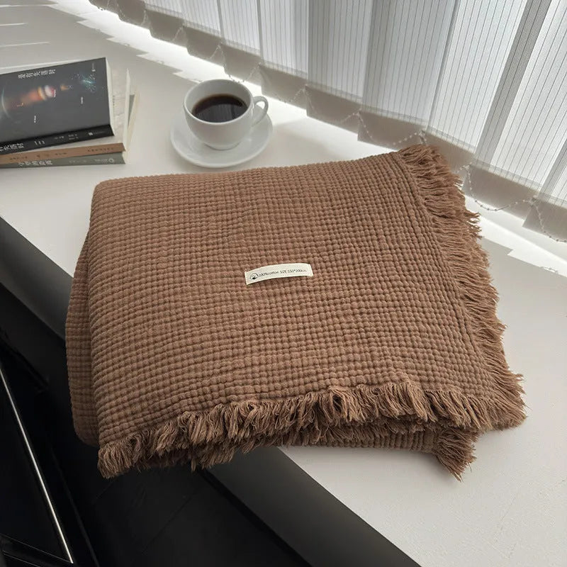 Four-layer cotton gauze blanket with tassel trim in avocado green colour laid flat.