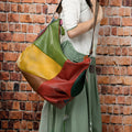 Brown cowhide leather crossbody travel bag showing front view with strap, holding a laptop and magazine.