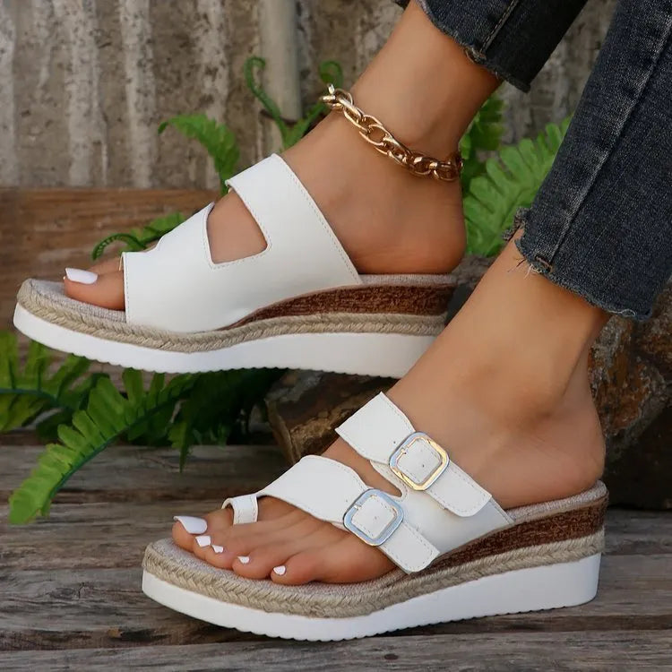 White wedge sandals with woven patent leather upper and open toe design on wooden surface