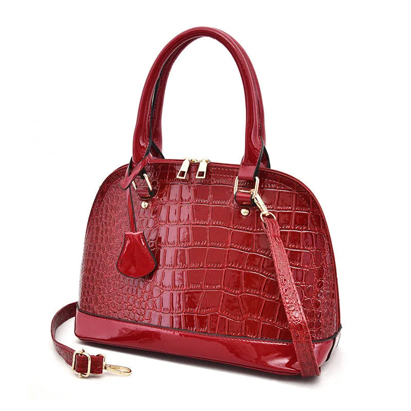 Large shiny black PU leather crossbody bag showing structured shell shape and shoulder strap.