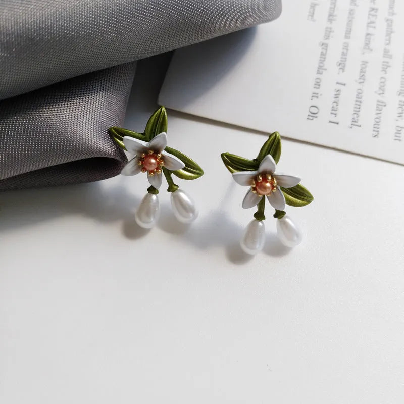 Close-up of women's camellia flower ear clip earrings with sterling silver needle accents on a contrasting background.