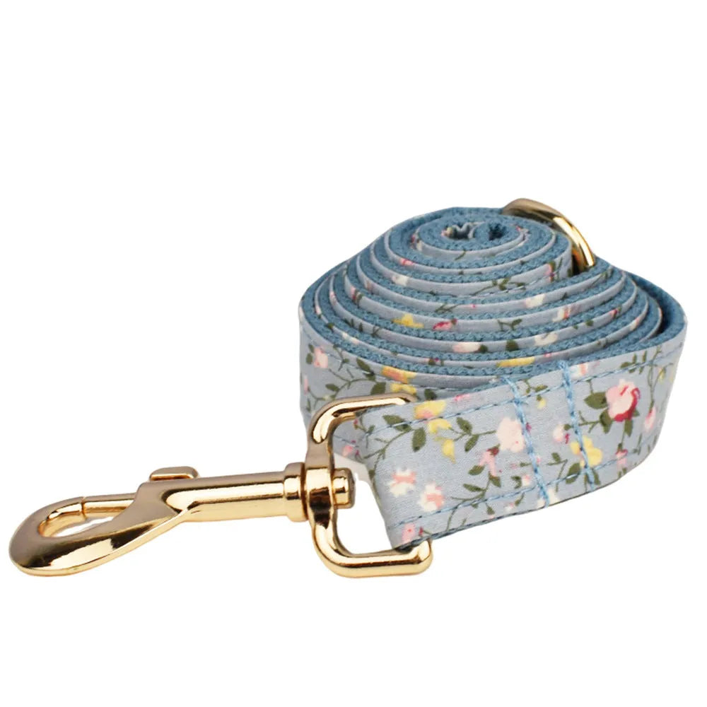 Blue floral patterned dog collar and matching leash, vest, and bow set on a white background.