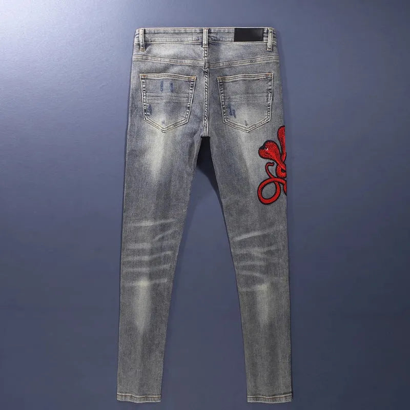 Slim fit blue jeans with distressed hole patches and embroidery on the legs, showing a washed-out colour.