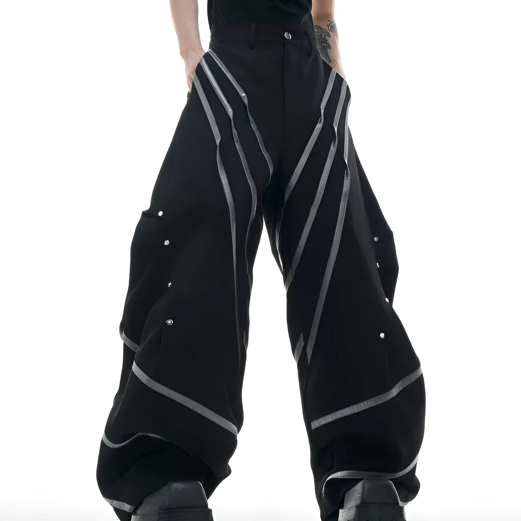 Men's black trousers with metal rivet pleats and a tapered leg, showing three-dimensional cutting.