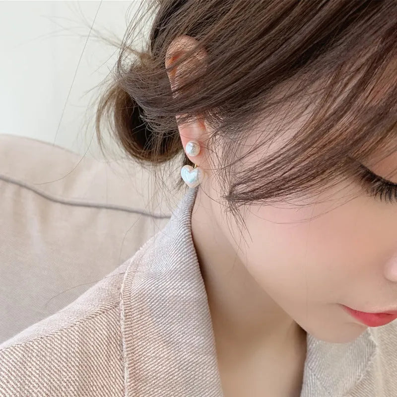 Close-up of women's silver-toned heart-shaped stud earrings with a central inlaid artificial pearl or gemstone.