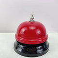 Iron call bell on a desk, shown in one of twelve available colours including red, blue, green, and pink.