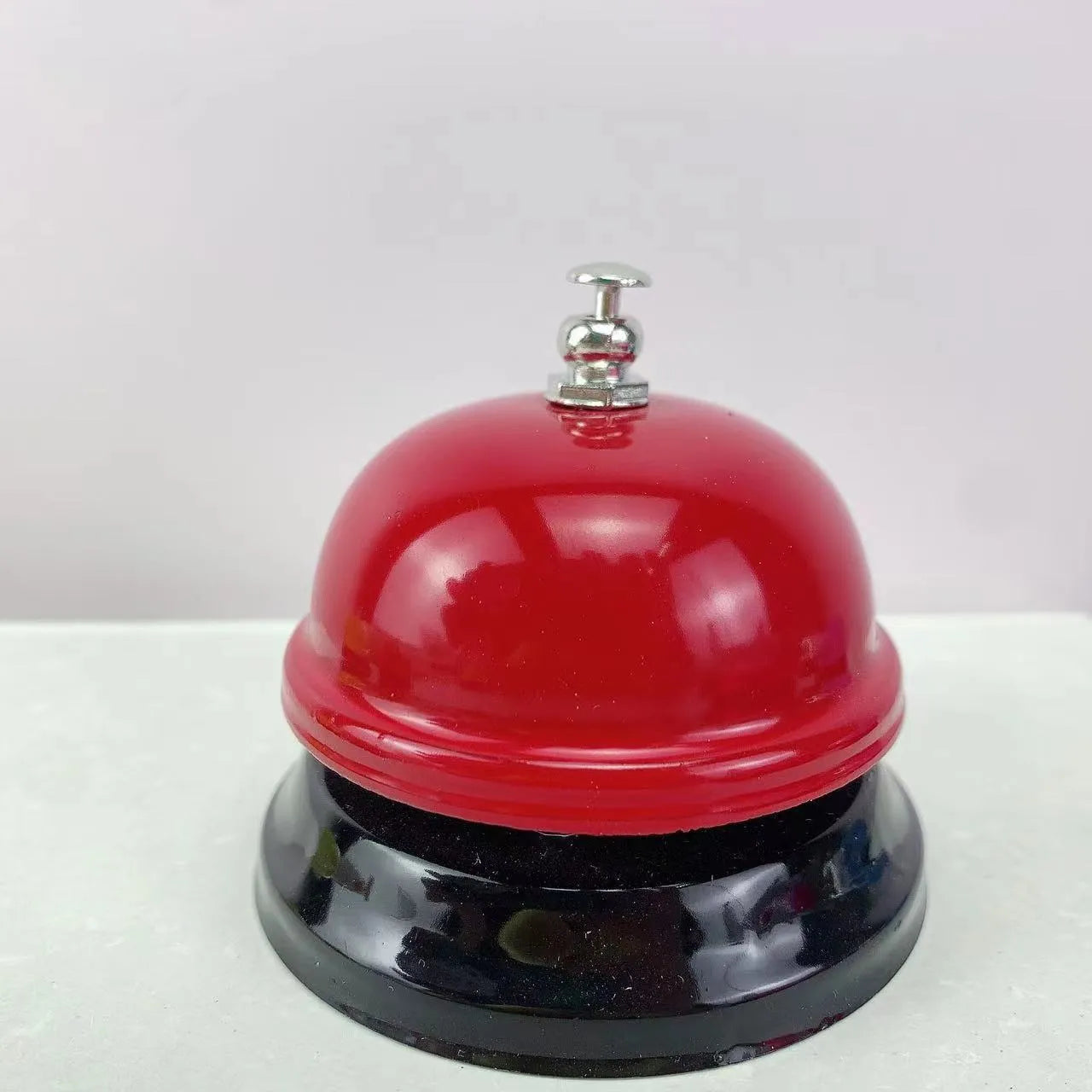 Iron call bell on a desk, shown in one of twelve available colours including red, blue, green, and pink.