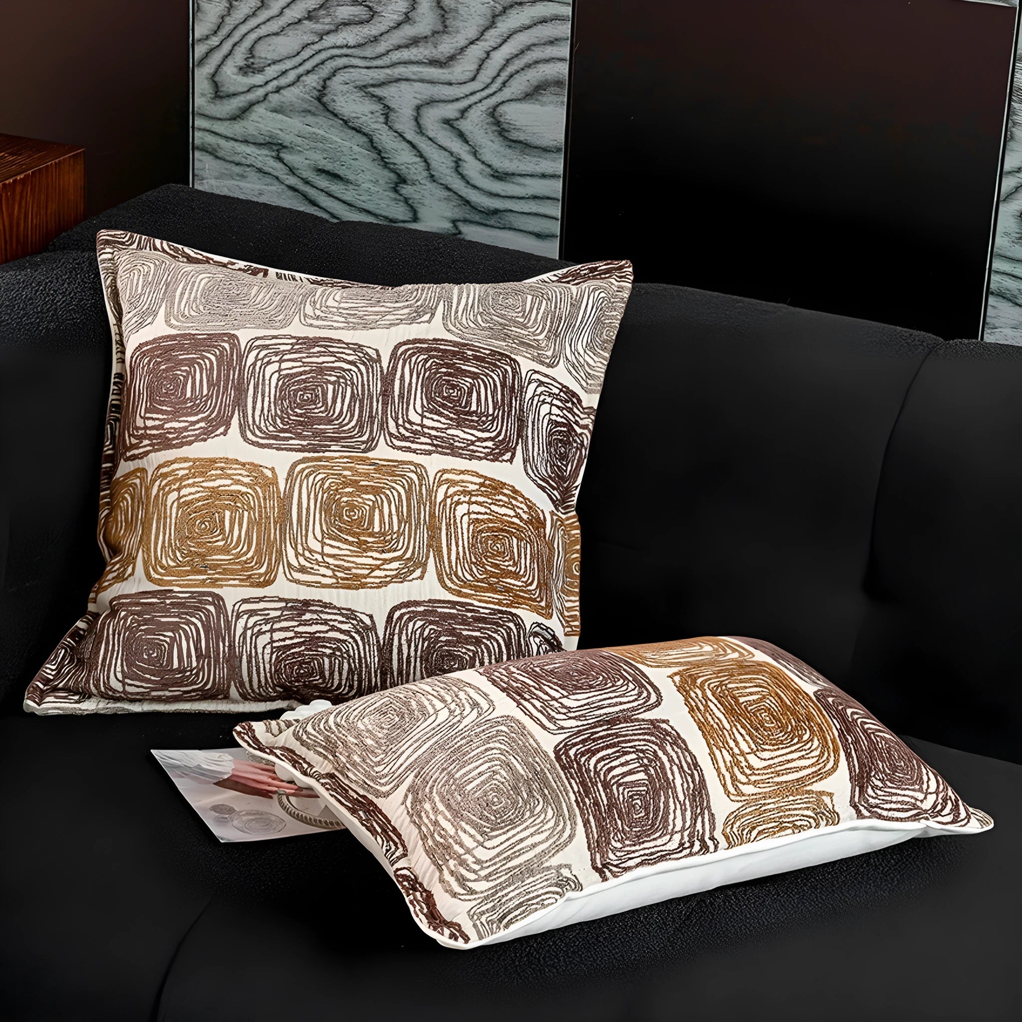 Cream and coffee-coloured abstract coil pattern on two pillow covers: one square, one rectangular.