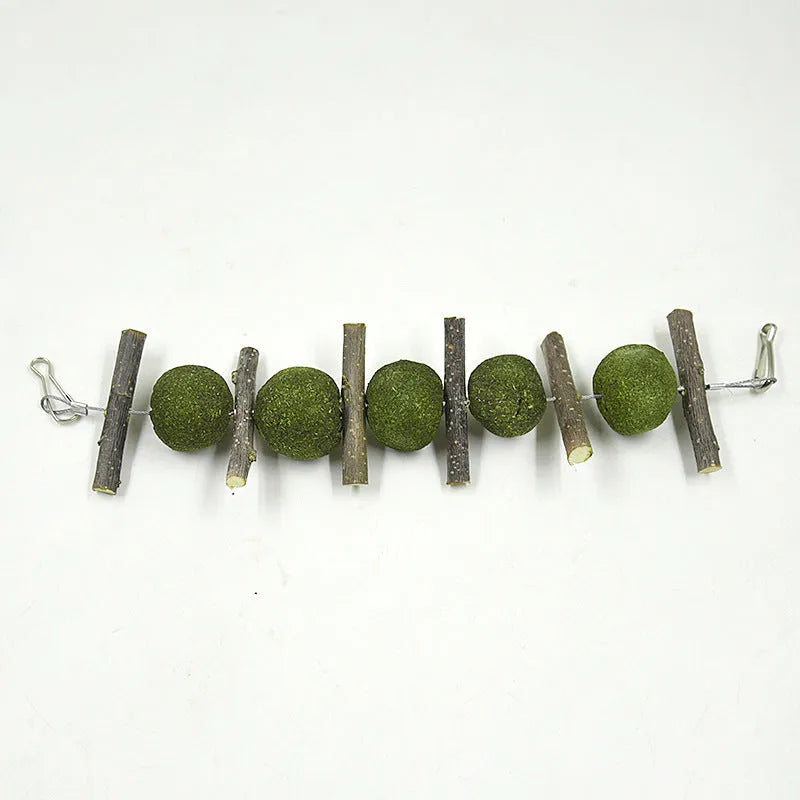 Natural grass balls and apple branches hanging chew toys for small pets on a cage bar