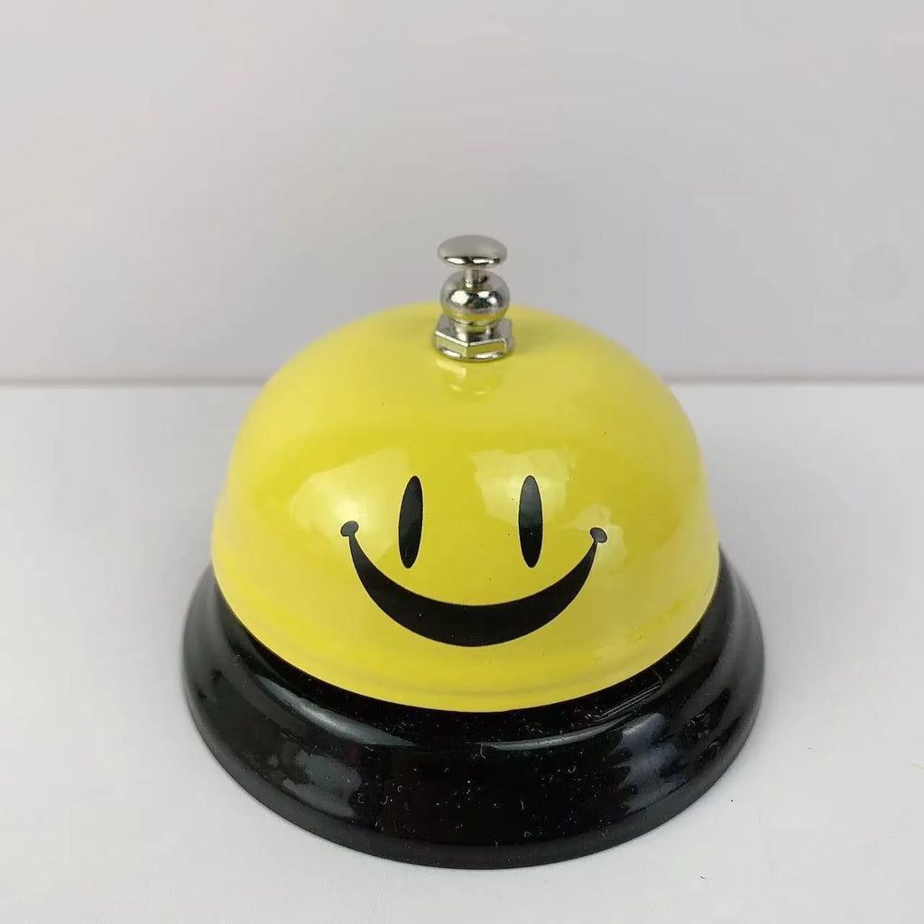 Iron call bell on a desk, shown in one of twelve available colours including red, blue, green, and pink.
