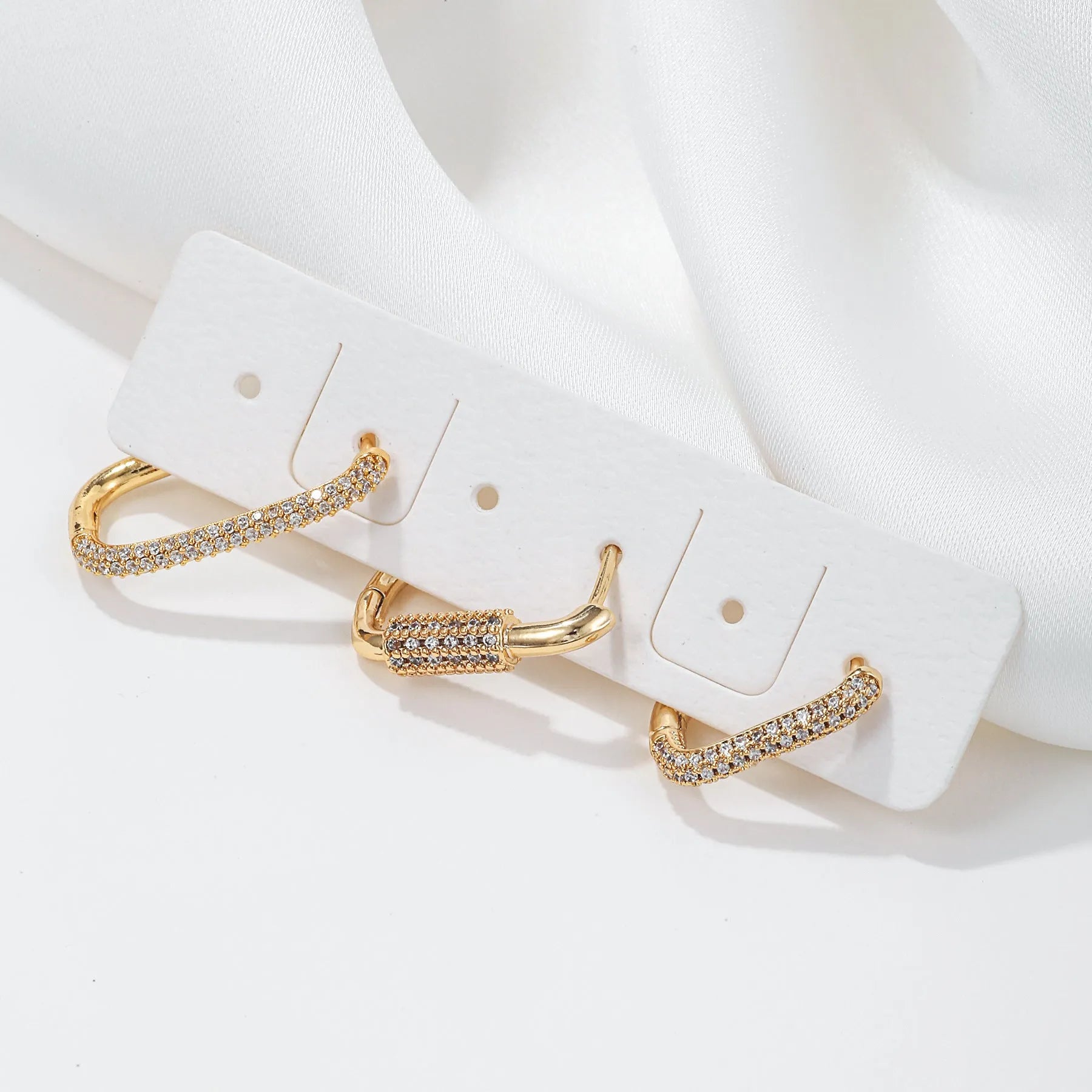 Three geometric ear clips with micro-inlaid zircon stones on copper, showing gold and white gold colour options
