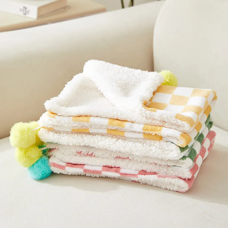 Green plaid patterned soft fleece pet blanket on a sofa, showing fur ball decoration.