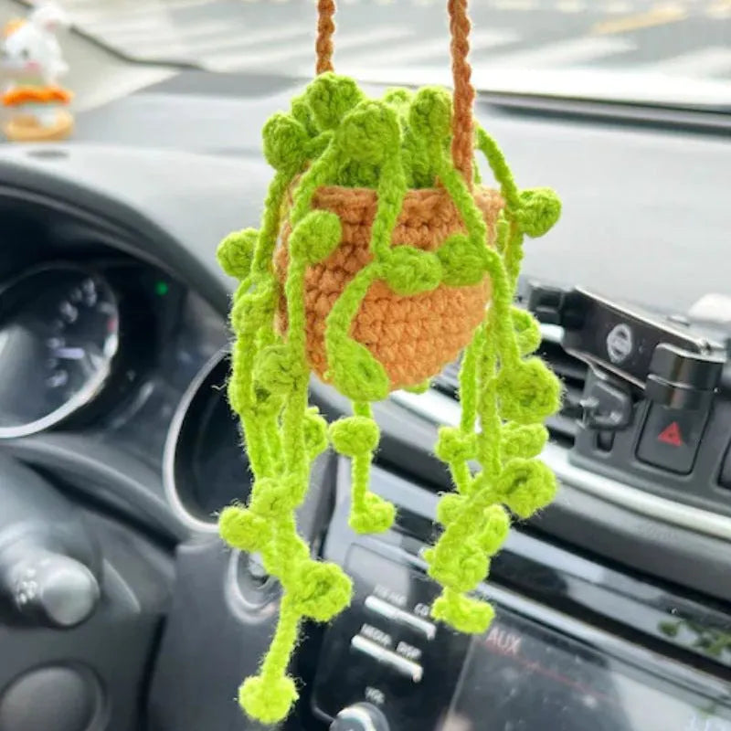 Green and white knitted wool car plant decoration hanging from a rope.