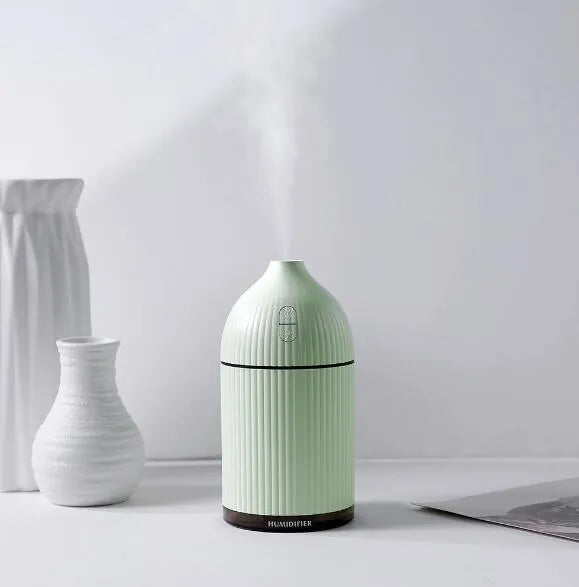 White ultrasonic aromatherapy diffuser and humidifier with 300ml capacity, USB port, and LED light on a wooden surface.