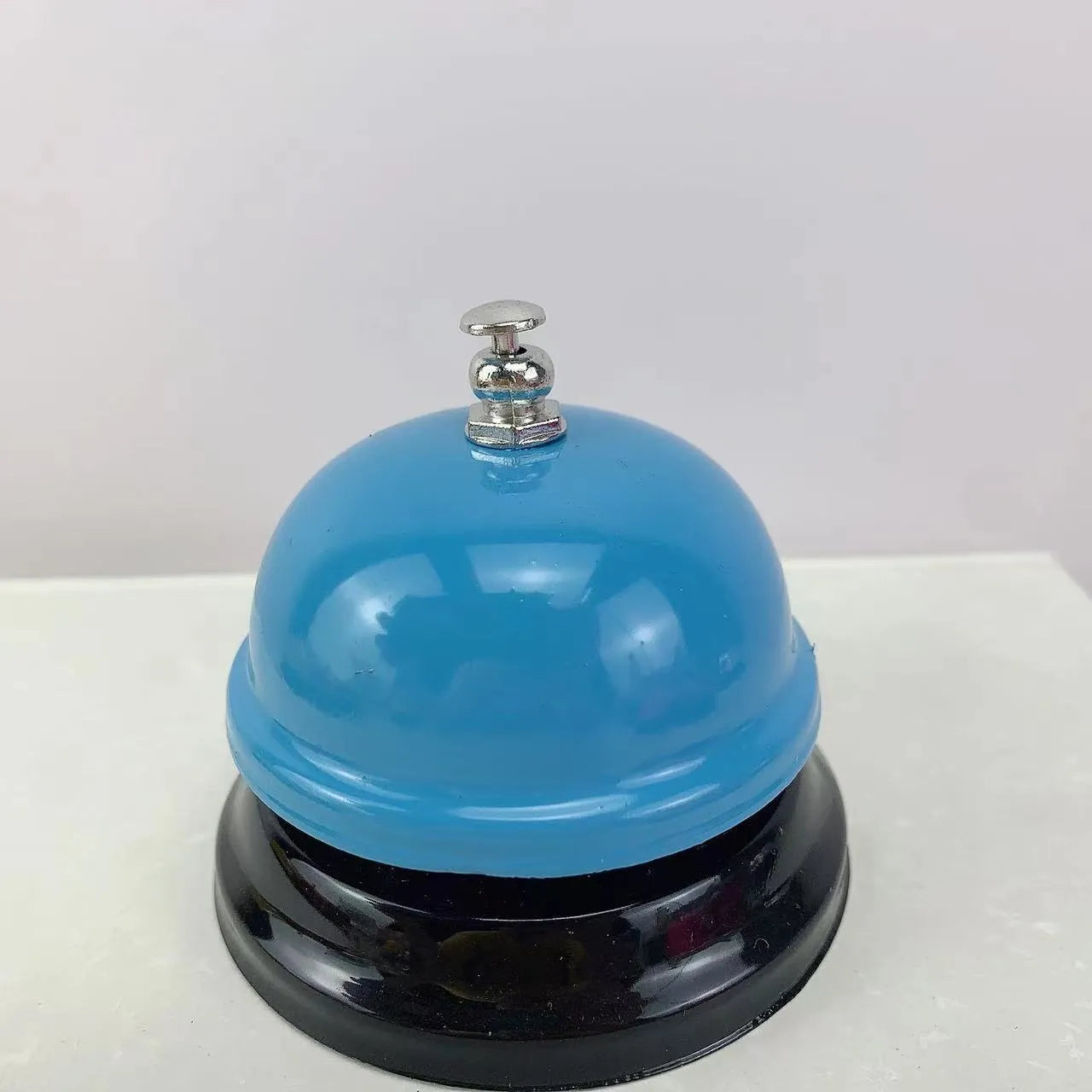 Iron call bell on a desk, shown in one of twelve available colours including red, blue, green, and pink.