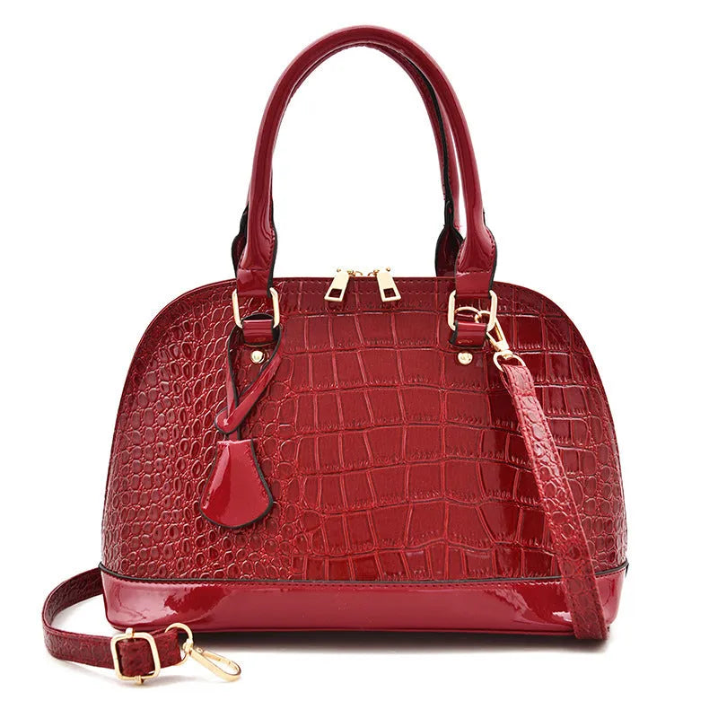 Large shiny black PU leather crossbody bag showing structured shell shape and shoulder strap.