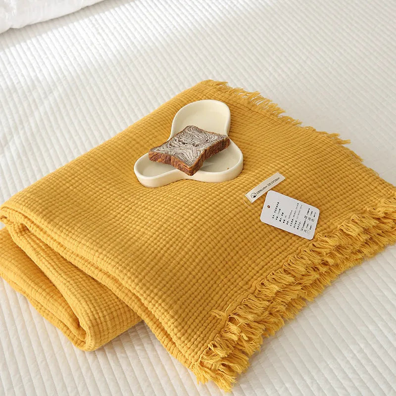 Four-layer cotton gauze blanket with tassel trim in avocado green colour laid flat.
