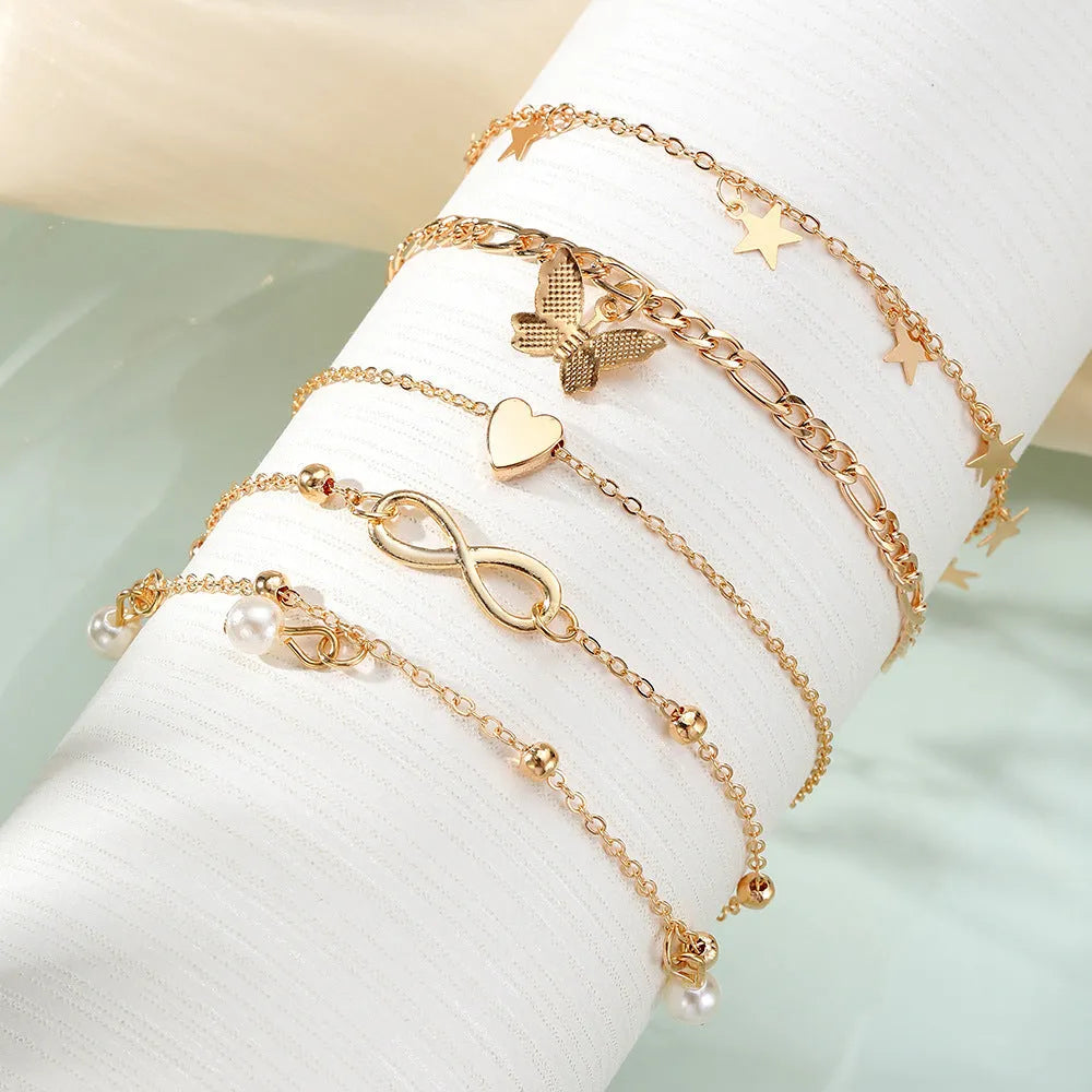 Four different alloy anklets with butterfly and pearl heart pendants arranged as a jewellery set