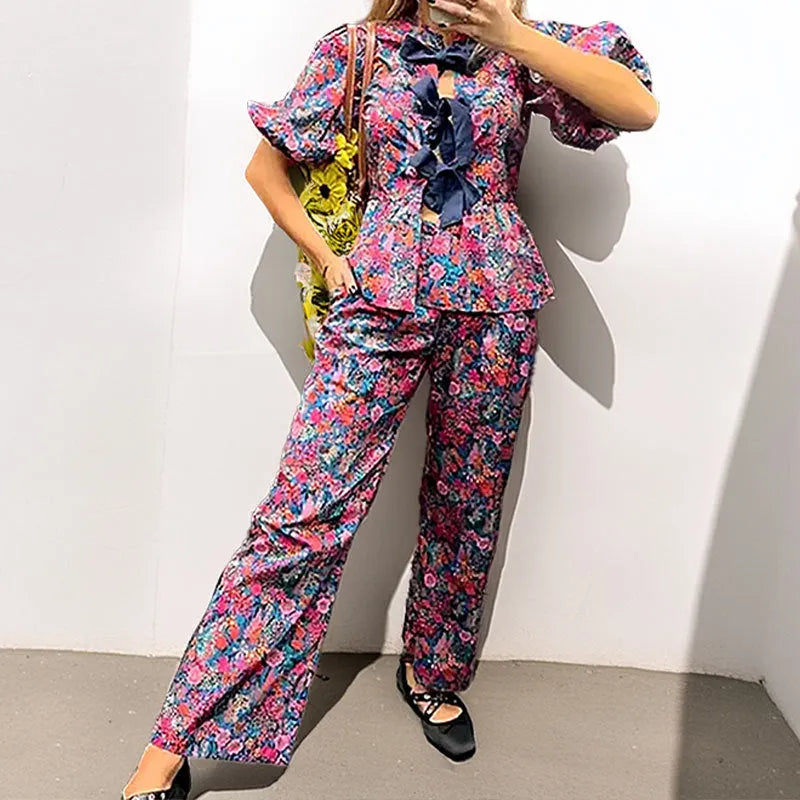Women's floral print tie-neck blouse and trousers suit with puff sleeves.