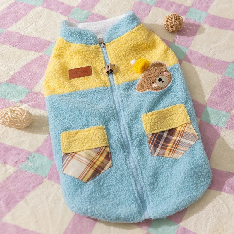 Small dog wearing a blue fleece jacket with bear embroidery and plaid pockets