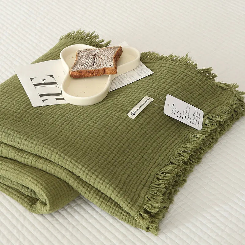 Four-layer cotton gauze blanket with tassel trim in avocado green colour laid flat.