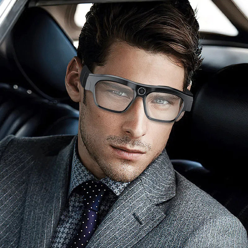 Black head-mounted smart Bluetooth glasses with a built-in camera for video recording on a table with accessories.