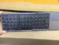 Black tri-fold folding Bluetooth keyboard with touchpad, shown both folded and unfolded.