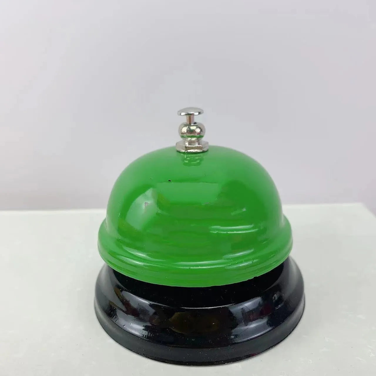 Iron call bell on a desk, shown in one of twelve available colours including red, blue, green, and pink.