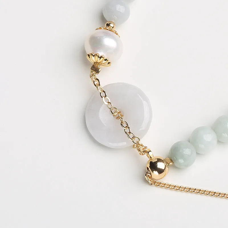 Close-up of a green jade and pearl bracelet with a geometric peace buckle on an elastic band.