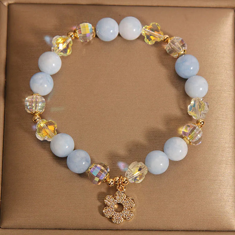 Women's aquamarine crystal bracelet with a four-leaf clover charm and pearl details on a white background