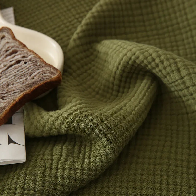 Four-layer cotton gauze blanket with tassel trim in avocado green colour laid flat.