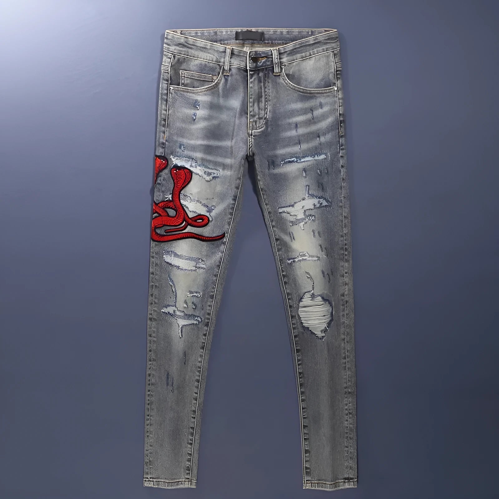 Slim fit blue jeans with distressed hole patches and embroidery on the legs, showing a washed-out colour.