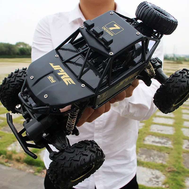 Large black and silver 4WD remote control off-road climbing cars with wireless controller on a rocky surface.