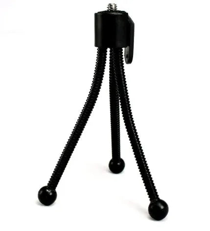 Small black iron mini tripod with ball head extended, next to an iPhone on a desk