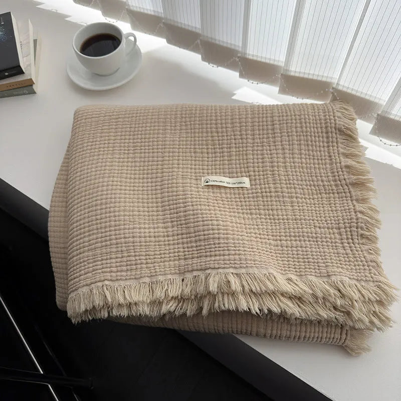 Four-layer cotton gauze blanket with tassel trim in avocado green colour laid flat.