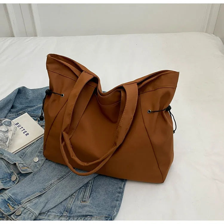 Soft Oxford cloth folding commuter tote bag shown in one of five colours: black, brown, dark grey, light grey or purple.